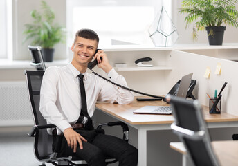 young man in a white shirt with a black tie at the table in a bright office calls