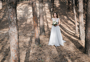 Wall Mural - A beautiful, satisfied bride in a pine forest poses.