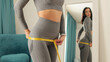 © shevtsovy - slim Woman waist Measuring With Tape at home. Beautiful woman checking success of weight loss program and measuring body in living room. slimming and weight loss concept.