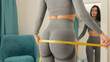 © shevtsovy - happy Woman Measuring body With Tape after weight loss fitness workout. Beautiful smiling woman measuring butt in front of mirror in living room after fitness marathon