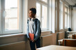 Pensive black schoolboy looks through the window in the classroom.