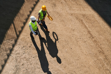 Contemplative modern constructors in safety vests and hardhats working on new house and discussing building process