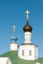 Two Orthodox Golden Bright Shiny Crosses Are On Top Of The Black And Blue Cupolas Of White Old Stone Church With A Green Roof