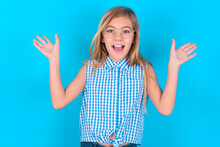 Little Kid Girl With Glasses Wearing Plaid Shirt Over Blue Background Raising Hands Up, Having Eyes Full Of Happiness Rejoicing His Great Achievements. Achievement, Success Concept.