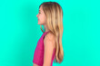 Profile of smiling blonde little kid girl wearing pink sport clothes over green background with healthy skin, has contemplative expression, ready to have outdoor walk.
