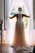 blonde Braut mit langem rosafarbenen Brautkleid stehend am Fenster mit Blick nach vorn