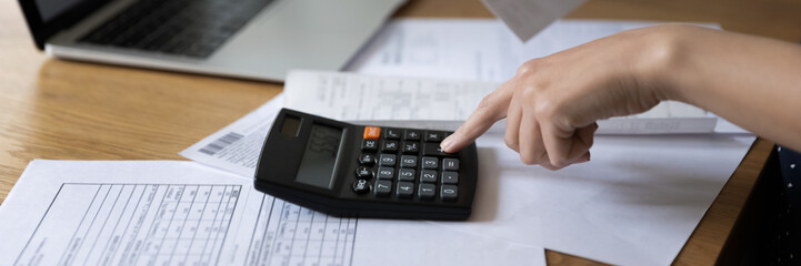 Panoramic horizontal cropped image unrecognizable female hand using calculator, table with heap of bills close up photo. Personal budget control, family finances management, pay bills, savings concept