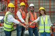 Group of Engineers smiling wear safety vests with helmets join hands to collaborate with team working in factory