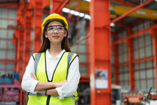 Portrait Of Young Female Engineer In Safety Vest And Glasses With Yellow Helmet Standing Arms Crossed Ready For Working In Factory