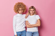 Upset gloomy female friends look frustrated have grumpy expressions wear casual clothes express negative emotions isolated over pink background. Worried discontent young women have problems.