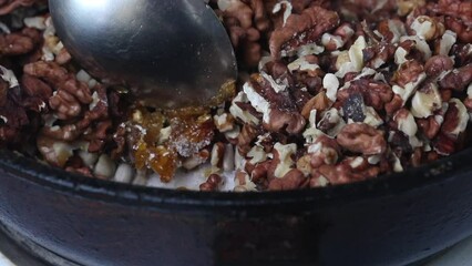 Poster - A woman prepares kozinak from nuts. Roasts sunflower seeds, peanuts and walnuts in sugar and honey. Close-up.