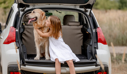 Preteen girl with golden retriever dog in car trunk