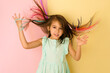 A happy girl throws multicolored strands of hair up with  hands, isolated on a pink-yellow studio backgraund. Developing curls. Healthy dyed strong hair. Natural dyes and tonics for hair without harm