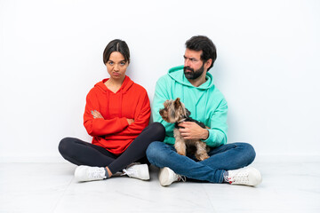 Wall Mural - Young caucasian couple sitting on the floor with their pet isolated on white background annoyed angry in furious gesture