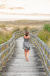Blonde Caucasian woman walking barefoot down wooden walkway wearing short printed dress