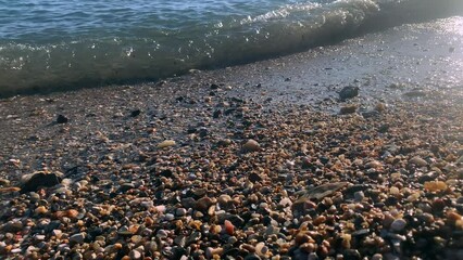 Poster - pebbles beach in sun rays small sea waves seascape rays of the setting sun light on beach