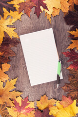 Wall Mural - Autumn leaves and notepad disposed on wooden table in the background. View from above.