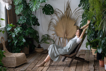 Relaxed calm woman florist rest in indoor garden breathing fresh air. Happy gardener girl enjoy mental balance and wellbeing in home greenhouse. Satisfied young lady taking pleasure of stress relief