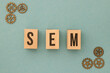 SEO - Search Engine Marketing letters made out of wood on the turquoise background with metal gears on the side