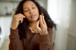 © Anatoliy Karlyuk - Selective focus on hand with transparent yellow vitamin pill of polyunsaturated fat acids or omega-3 fish oil, blurred puzzled and thoughtful face expression of African American female on background