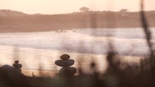 Rock Balancing On Pebble Beach, Monterey 17-mile Drive, California Coast, USA. Stable Pyramid Stacks Of Round Stones, Sea Ocean Water Waves Crashing At Sunset. Serenity Harmony, Calm Zen Meditation.