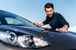 Handsome bearded man in casual wear washing car doors and hood