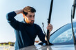 Bearded man feeling confused while changing windscreen wipers on a car