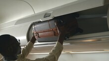 Passenger Black Man Putting Luggage On Top Shelf Or Cabin Compartment On Airplane