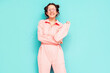 Young beautiful smiling female in trendy summer pink overalls. Sexy carefree woman posing near blue wall in studio with two horns. Positive model having fun and going crazy. Cheerful and happy