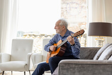 Senior Man Playing Guitar Sitting On Sofa In Living Room At Home