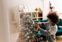 Smiling Afro Woman Decorating Christmas Tree With Bauble In Living Room At Home