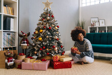 Happy Woman Sitting With Gifts By Christmas Tree At Home