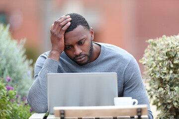 Concerned man with black skin using laptop in a bar