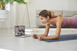 © Studio Romantic - Determined active young woman doing sports workout on floor mat at home, watching online video, following professional athlete's instructions, practicing calorie burning forearm elbow plank exercise