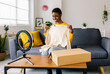 Smiling african american blogger influencer recording video communication with subscribers at home. Young happy woman unpacking parcel and smiling to the smartphone camera