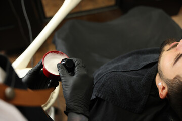 Wall Mural - Professional hairdresser with shaving foam near bearded client in barbershop, closeup