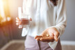 © Dragana Gordic - Close up photo of one round white pill in young female hand. Woman takes medicines with glass of water. Daily norm of vitamins, effective drugs, modern pharmacy for body and mental health concept