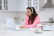 © New Africa - African American woman with modern laptop and headphones studying in kitchen. Distance learning