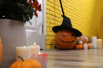 Wall Mural - Pumpkin with drawn creepy face and burning candles near yellow brick wall in hallway. Halloween decor