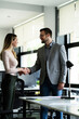 © JustLife - Colleagues heandshake in office. Businesswoman and businessman discussing work in office