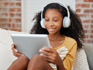 Wall Mural - What my school holiday looks like. Shot of a girl using a tablet while sitting on the couch at home.