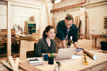 Weve got plenty of work to do today. Cropped shot of two young carpenters using a laptop and digital tablet working together inside their workshop.