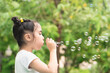 Cute little girl playing, blowing bubble in outdoor summer city park