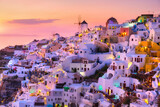 Fototapeta Uliczki - Oia village, Santorini, Greece. View of traditional houses in Santorini. Small narrow streets and rooftops of houses, churches and hotels. Landscape during sunset.