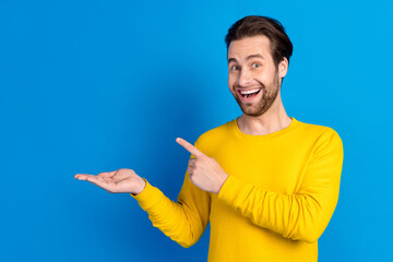 Poster - Portrait of attractive cheerful amazed brunet guy demonstrating on palm copy space offer ad isolated over bright blue color background