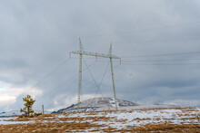High Voltage Power Line In The Mountains With Snow On Mountains And Dry Meadows Close Up