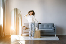 Carefree Joyful African American Girl Jumping Dancing Alone Moving To Rhythm In Living Room, Happy African American Young Woman Have Fun Enjoying Listening To Music, Entertain On Weekend At Home