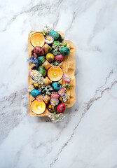 Wall Mural - Beautiful Easter composition. carton box with colorful eggs, diy candles in eggs shells, flowers on marble background. festive spring season. table decor for Easter holiday, Ostara sabbat. top view