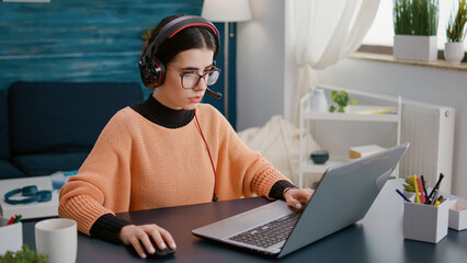 Wall Mural - Young woman attending video call meeting on laptop with headphones, talking on remote teleconference for school class work. Female student using headset and computer on videoconference.