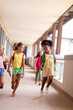 Full length of cheerful multiracial elementary schoolgirls walking in corridor